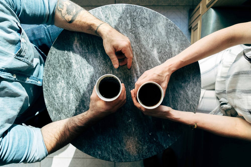 A photo shot from above of two people drinking coffee and talking at a table